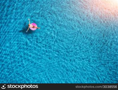 Aerial view of young woman swimming on the pink swim ring in the transparent blue sea at sunset. Summer aerial landscape with girl, clear water in the evening. Top view. Travel and holiday in Europe. Summer aerial landscape with girl, clear water in the evening