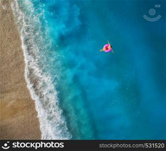 Aerial view of young woman swimming on the pink swim ring in the transparent turquoise sea in Oludeniz,Turkey. Summer seascape with girl, beautiful waves, blue water in sunny day. Top view from drone. Aerial view of young woman swimming on the pink swim ring