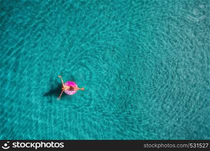 Aerial view of young woman swimming on the pink swim ring in the transparent turquoise sea in Blue Lagoon in Oludeniz,Turkey. Summer seascape with girl, azure water in the morning. Top view from drone. Aerial view of young woman swimming on the pink swim ring
