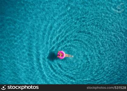 Aerial view of young woman swimming on the pink swim ring in the transparent turquoise sea in Blue Lagoon in Oludeniz,Turkey. Summer seascape with girl, azure water in the morning. Top view from drone. Aerial view of young woman swimming on the pink swim ring