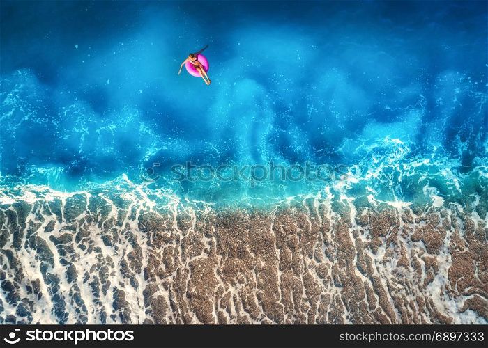 Aerial view of young woman swimming on the pink swim ring in the transparent turquoise sea in Oludeniz,Turkey. Summer seascape with girl, beautiful waves, azure water at sunset. Top view from drone