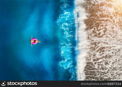 Aerial view of young woman swimming on the pink swim ring in the transparent turquoise sea in Oludeniz,Turkey. Summer seascape with girl, beautiful waves, azure water in sunny day. Top view from drone
