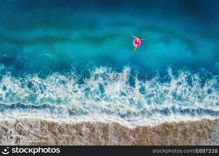 Aerial view of young woman swimming on the pink swim ring in the transparent turquoise sea in Oludeniz,Turkey. Summer seascape with girl, beautiful waves, azure water at sunset. Top view from drone
