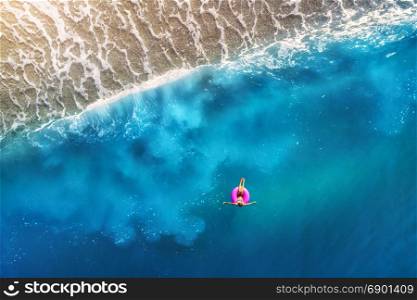 Aerial view of young woman swimming on the pink swim ring in the transparent turquoise sea in Oludeniz,Turkey. Summer seascape with girl, beautiful waves, blue water at sunset. Top view from drone