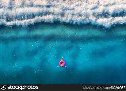 Aerial view of young woman swimming on the pink swim ring in the transparent turquoise sea in Oludeniz,Turkey. Summer seascape with girl, beautiful waves, blue water at sunrise. Top view from drone. Aerial view of young woman swimming in the sea