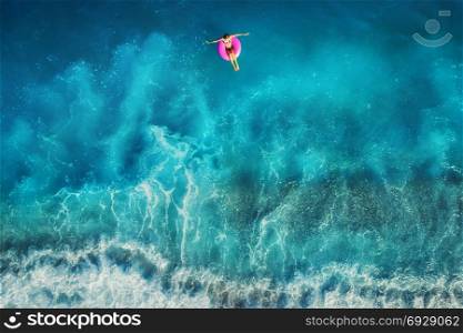 Aerial view of young woman swimming on the pink swim ring in the transparent turquoise sea in Oludeniz,Turkey. Summer seascape with girl, beautiful waves, azure water at sunset. Top view from drone. Aerial view of young woman swimming on the pink ring