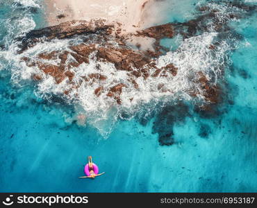 Aerial view of young woman swimming on the pink swim ring in the transparent turquoise sea in Maldives. Summer seascape with girl, beach, beautiful waves, rocks, blue water at sunset. Top view. Nature