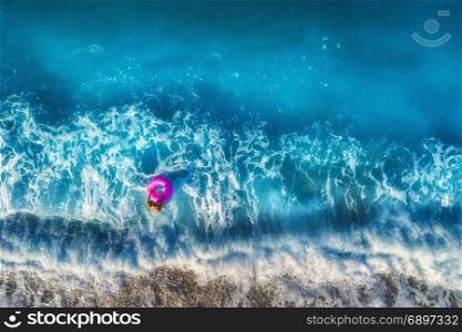 Aerial view of young woman with pink swim ring in the transparent turquoise sea in Oludeniz,Turkey. Summer seascape with girl, beautiful waves, blue water in sunny morning. Top view from drone. Travel