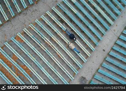 Aerial view on young couple lying on old wooden benches of outdoor theater on an autumn day 