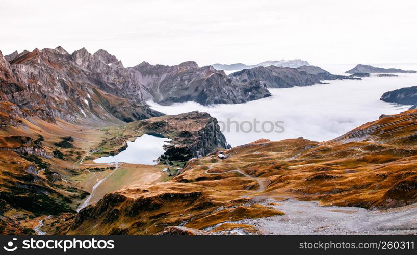 Aerial view over cloud, high grass land rocky alpine mountain valley and lake Trubsee of Titlis in Engelberg, Switzerland