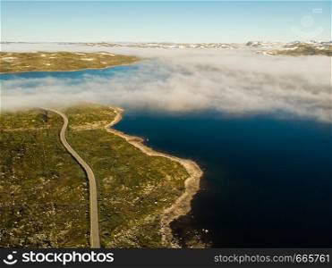 Aerial view. Road crossing Hardangervidda mountain plateau, clouds over lakes, morning time. Norway landscape. National tourist Hardangervidda route.. Road crossing Hardangervidda plateau, Norway. Aerial view.