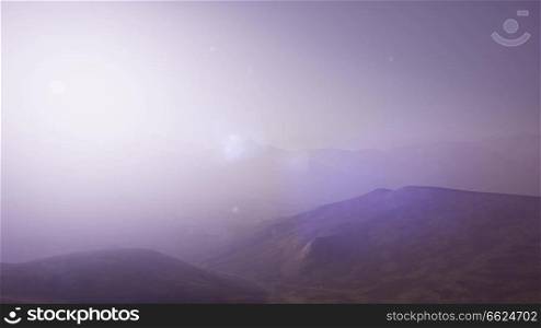 Aerial View. Sunset. Flight over a green grassy rocky hills. Aerial Green Hills Landscape in Fog