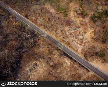 Aerial view, The road passes through a dry orange-yellow forest. Some parts were destroyed by a forest fire.