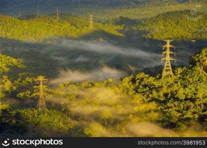 Aerial view Transmission tower in green forest and beautiful morning smooth fog. Energy and environment concept. High voltage power poles. Pang Puay, Mae Moh, Lampang, Thailand.. High voltage power poles in green forest with fog.