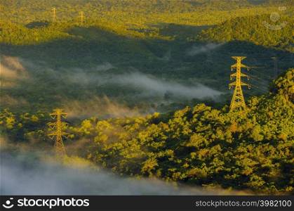 Aerial view Transmission tower in green forest and beautiful morning smooth fog. Energy and environment concept. High voltage power poles. Pang Puay, Mae Moh, Lampang, Thailand.. High voltage power poles in green forest with fog.
