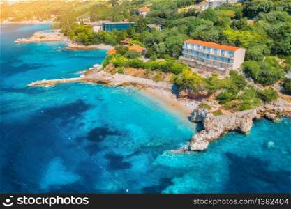 Aerial view with beautiful sea coast, sandy beach, clear blue water, hotels and green trees at sunset. Summer tropical landscape. Top view of blue sea, buildings, rocks and forest. Luxury resort. Aerial view with sea coast, sandy beach, blue water, hotels