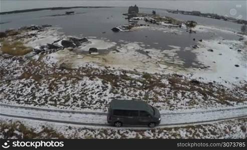 Aerial winter shot of a car driving in severe area. White Sea coast in winter with view to old wooden house and Rabocheostrovsk, township near Solovki