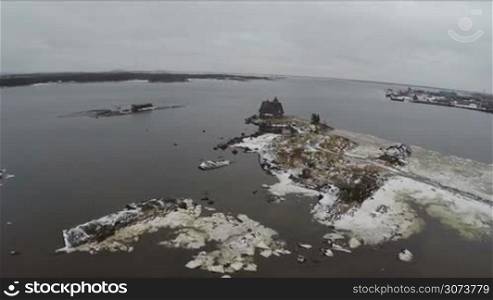 Aerial winter shot of moving closer to old wooden house or monastery located on the edge of White Sea coast. Rabocheostrovsk, territory by Solovki