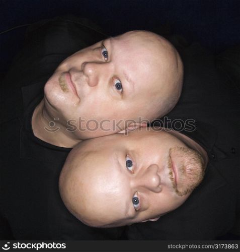 Aeriel view of Caucasian bald identical twin men sitting back to back and looking up at viewer.