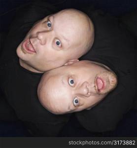 Aeriel view of Caucasian bald identical twin men sitting back to back making facial expressions.
