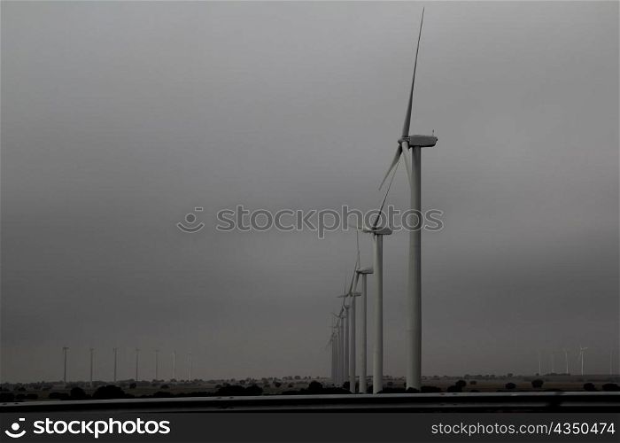 aerogenerator windmills in a row on cloudy gray day