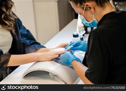 Aesthetician doing the manicure, filing the nails with a file to his client in a beauty center. Business and beauty concepts. Aesthetician doing the manicure, filing the nails with a file to his client in a beauty center