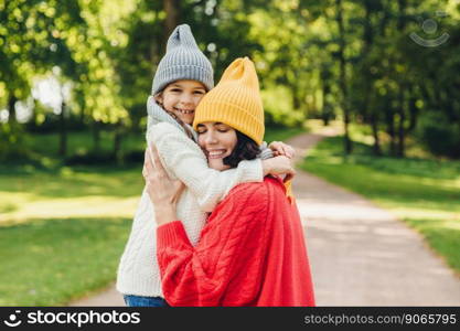 Affectionate good looking young mother embraces her single daughter, have warm relationship, being glad to have so clever and beautiful girl, play together outdoor, understand each other very well