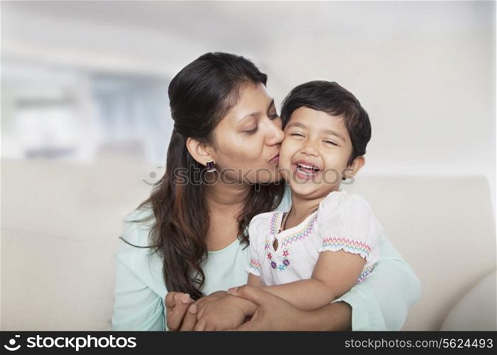 Affectionate mother holding and kissing her daughter on the couch