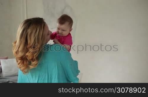 Affectionate mother nursing her little daughter. Loving mother carrying and kissing newborn child while relaxing in grunge styled bedroom. Happy family enjoying time together at home. Slow motion. Stedicam stabilized.shot.