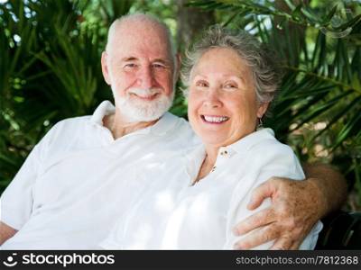 Affectionate senior couple in tennis whites, against a background of tropical palm fronds.