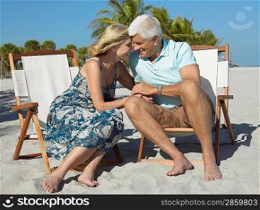 Affectionate senior couple on sunloungers on beach holding hands