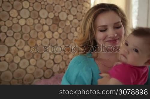 Affectionate yong mother carrying her infant child and rocking her to sleep while dancing in living room. Caring mother playing with her baby girl, spinning around and dancing in domestic interior. Slow motion. Steadicam stabilized shot.