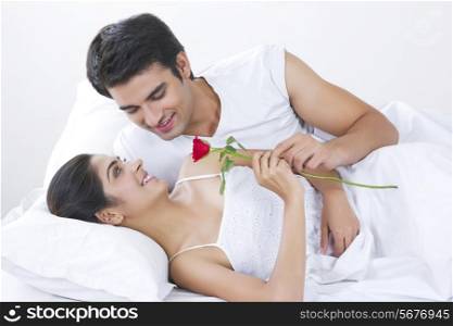 Affectionate young couple holding rose in bed