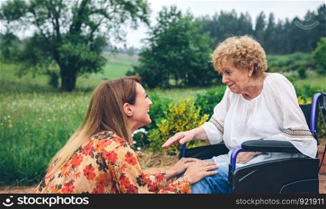 Affectionate young woman talking to elderly woman in a wheelchair in the garden. Young woman talking to elderly woman in a wheelchair