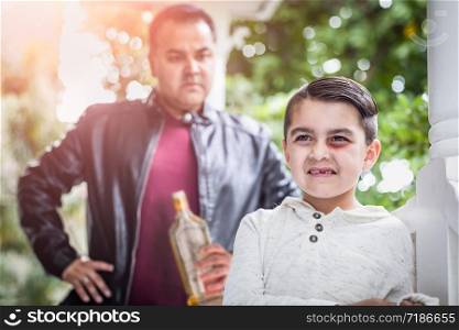 Afraid and Bruised Mixed Race Boy In Front of Angry Man Holding Bottle of Alcohol.