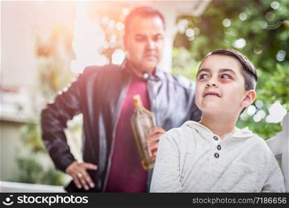 Afraid and Bruised Mixed Race Boy In Front of Angry Man Holding Bottle of Alcohol.