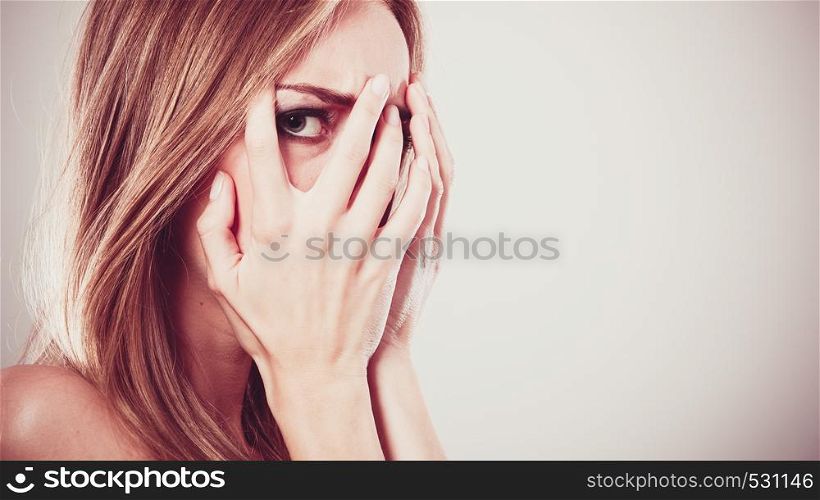 Afraid frightened woman peeking through her fingers on grey. Shy teen girl covering face with hands.