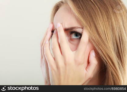 Afraid frightened woman peeking through her fingers on grey. Shy teen girl covering face with hands.