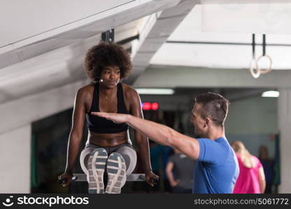 african american athlete woman workout out arms on dips horizontal parallel bars Exercise training triceps and biceps doing push ups with trainer