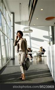 African American business woman with bag using mobile phone and walking in the office