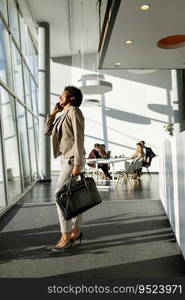 African American business woman with bag using mobile phone and walking in the office