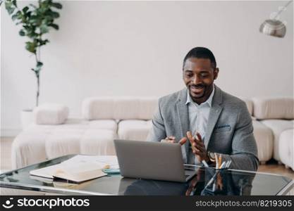 African american businessman communicates with client by video call, sitting at desk with laptop. Black male manager talks online with colleague or business partner, discussing working project.. African american businessman communicates with client by video call, sitting at desk with laptop