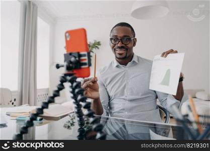 African american businessman showing economic statistics to coworkers, discussing project by video call, mobile phone app. Black male business coach shows graph, consulting client online.. African american businessman shows economic statistics, consulting client by video call, using phone