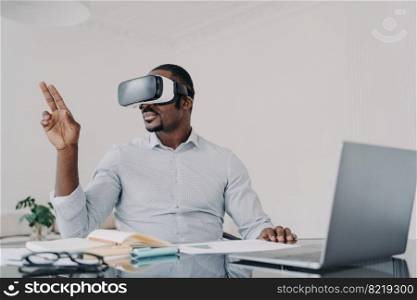African american businessman wearing vr glasses working on project in cyberspace at laptop. Black male manager works in augmented virtual reality, using high tech gadget for business at the workplace.. African american businessman in vr glasses working on business project in virtual reality at laptop