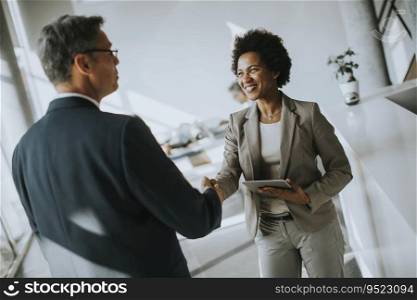 African American businesswoman holding digital tablet and looking at handsome colleague while shaking hands in office