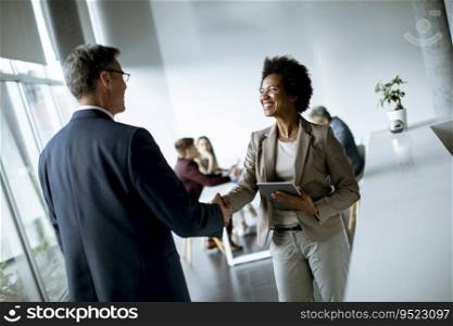 African American businesswoman holding digital tablet and looking at handsome colleague while shaking hands in office