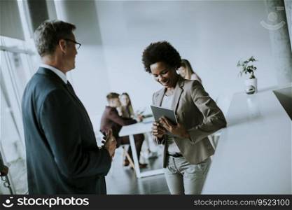 African American businesswoman holding digital tablet and talking with handsome colleague in office