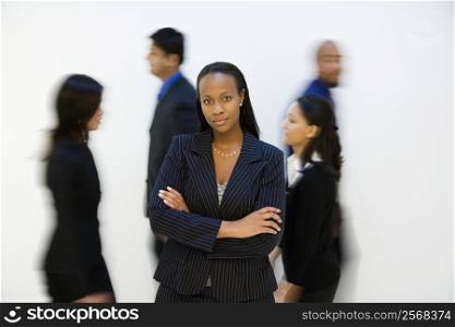 African-American businesswoman standing with arms crossed while others walk by.