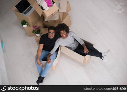 African American couple sitting in a box playing with packing material, having fun after moving in new home