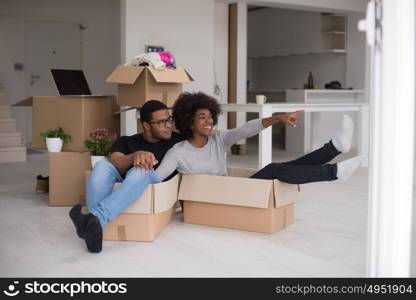 African American couple sitting in a box playing with packing material, having fun after moving in new home